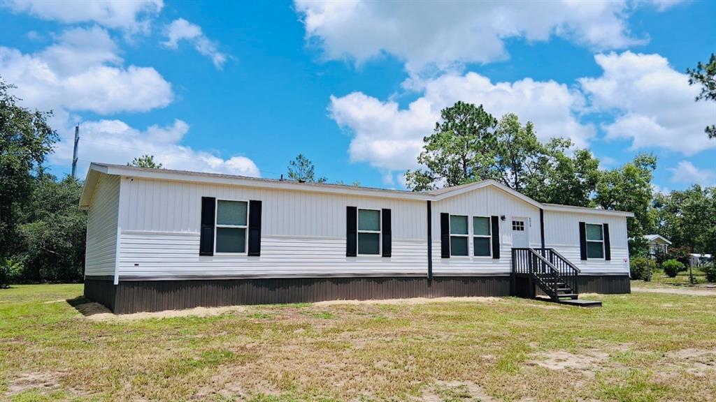 A single-story manufactured home with white vertical siding, dark shutters, and a small wooden porch — 6710 AUTUMNWOOD COURT, KEYSTONE HEIGHTS, FL