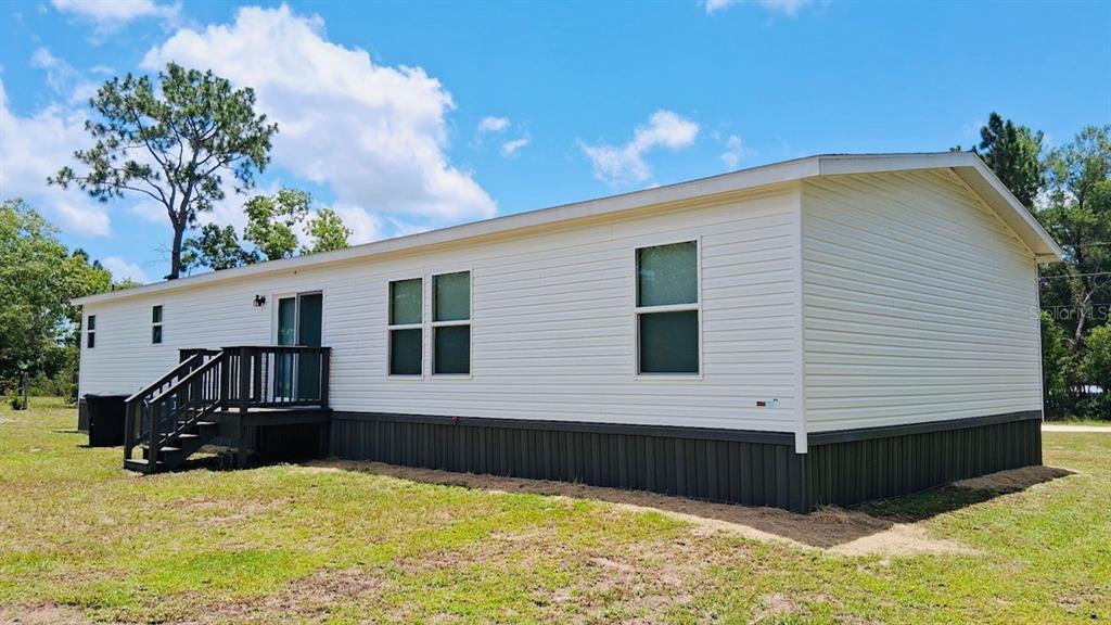 A single-story manufactured home with white siding, a dark skirt, and a wooden deck — 6710 AUTUMNWOOD COURT, KEYSTONE HEIGHTS, FL