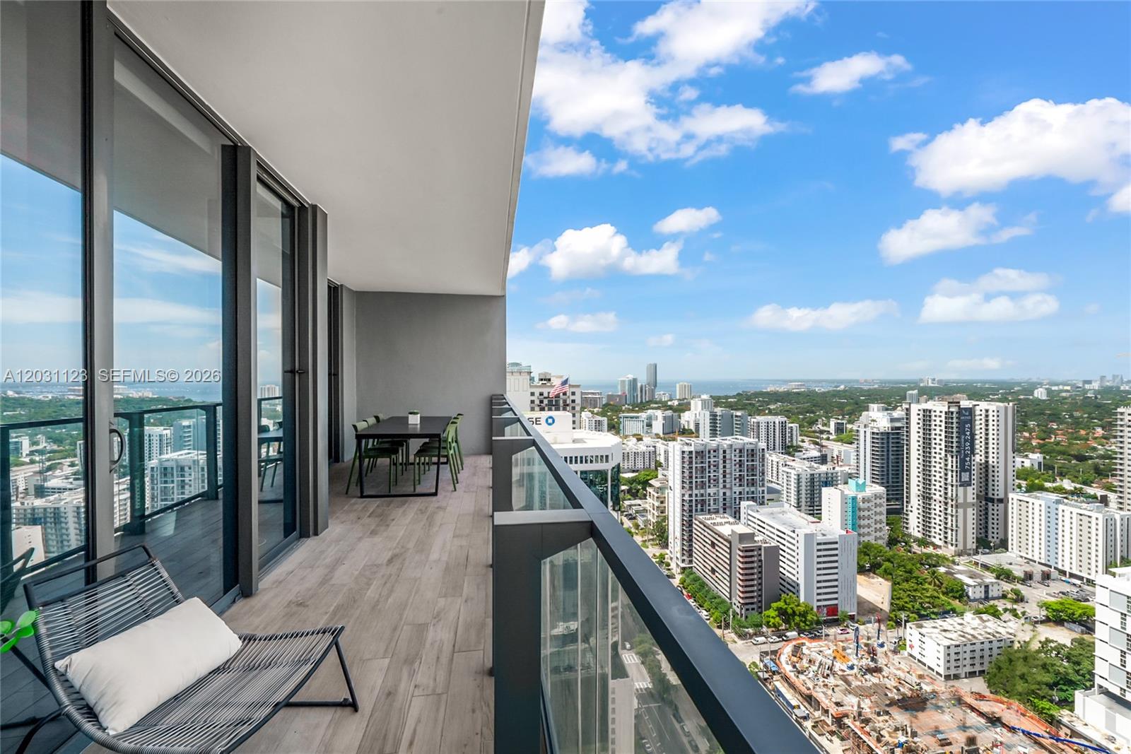 A high-rise balcony features wood-look flooring, a dining set, a lounge chair, and city views — 88 SW 7th St # 3208, Miami FL 33130, MIAMI, FL