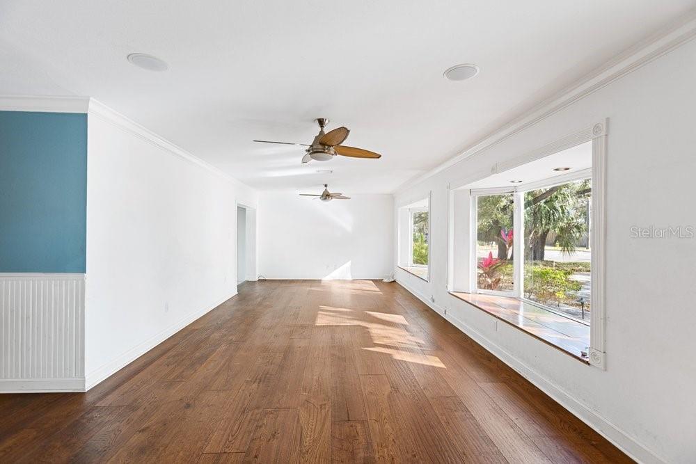 An empty living room features dark wood flooring, white walls, ceiling fans, and bay windows — 201 S SHERRILL STREET, TAMPA, FL