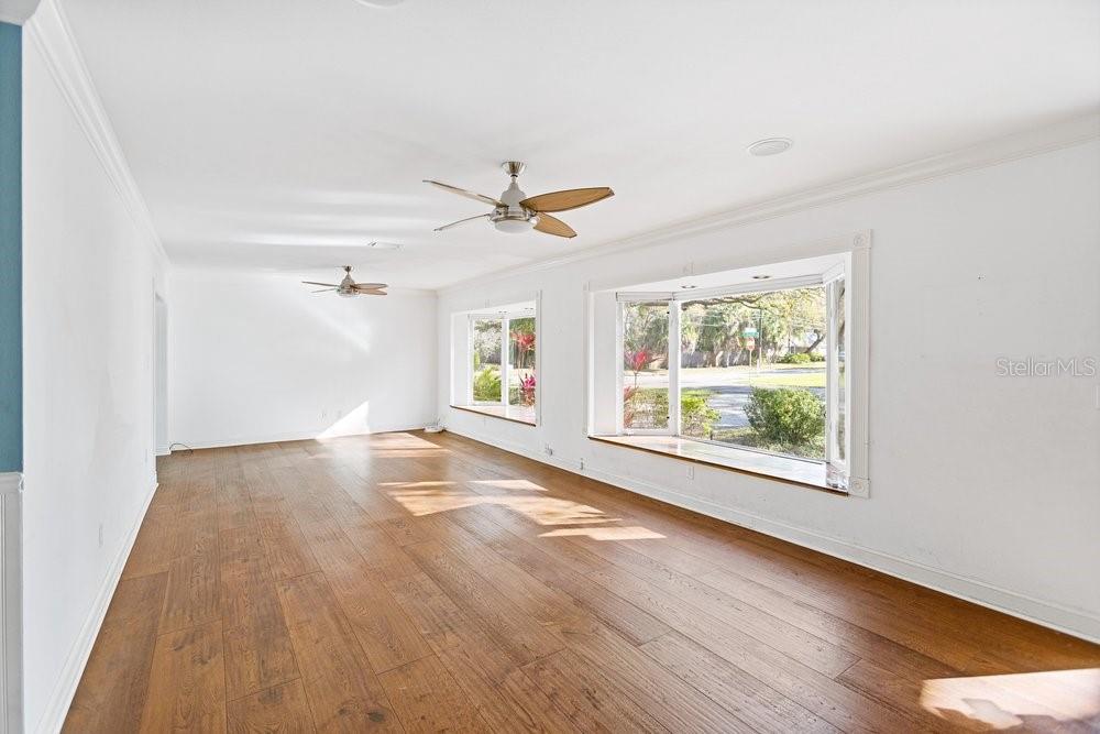 An empty room features hardwood floors, two ceiling fans, and two large bay windows — 201 S SHERRILL STREET, TAMPA, FL