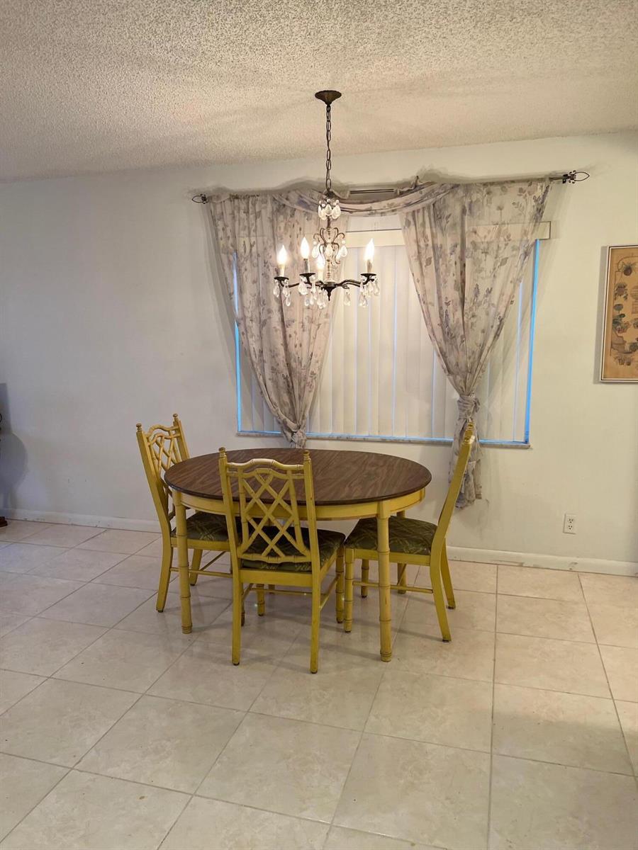A dining area features a round wooden table with yellow chairs under a crystal chandelier — 192 Flanders Drive, Delray Beach FL 33484, DELRAY BEACH, FL