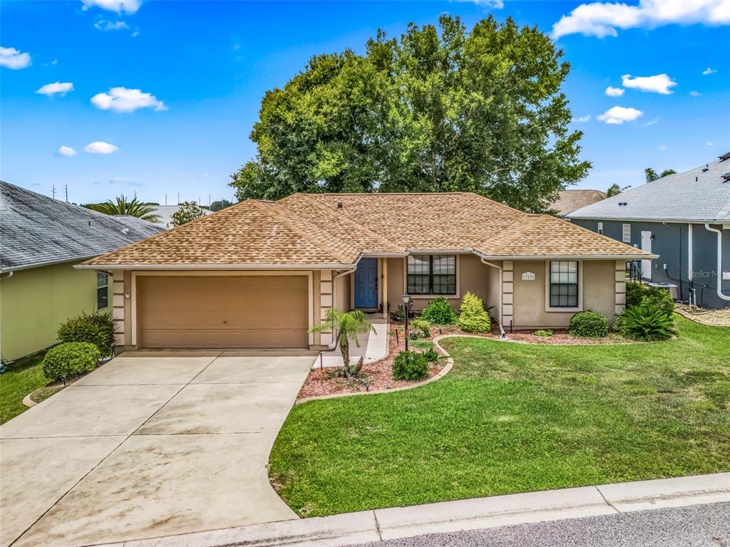 A single-story house with a tan stucco exterior, a brown shingled roof, and a concrete driveway — 17898 SE 125TH CIRCLE, SUMMERFIELD, FL