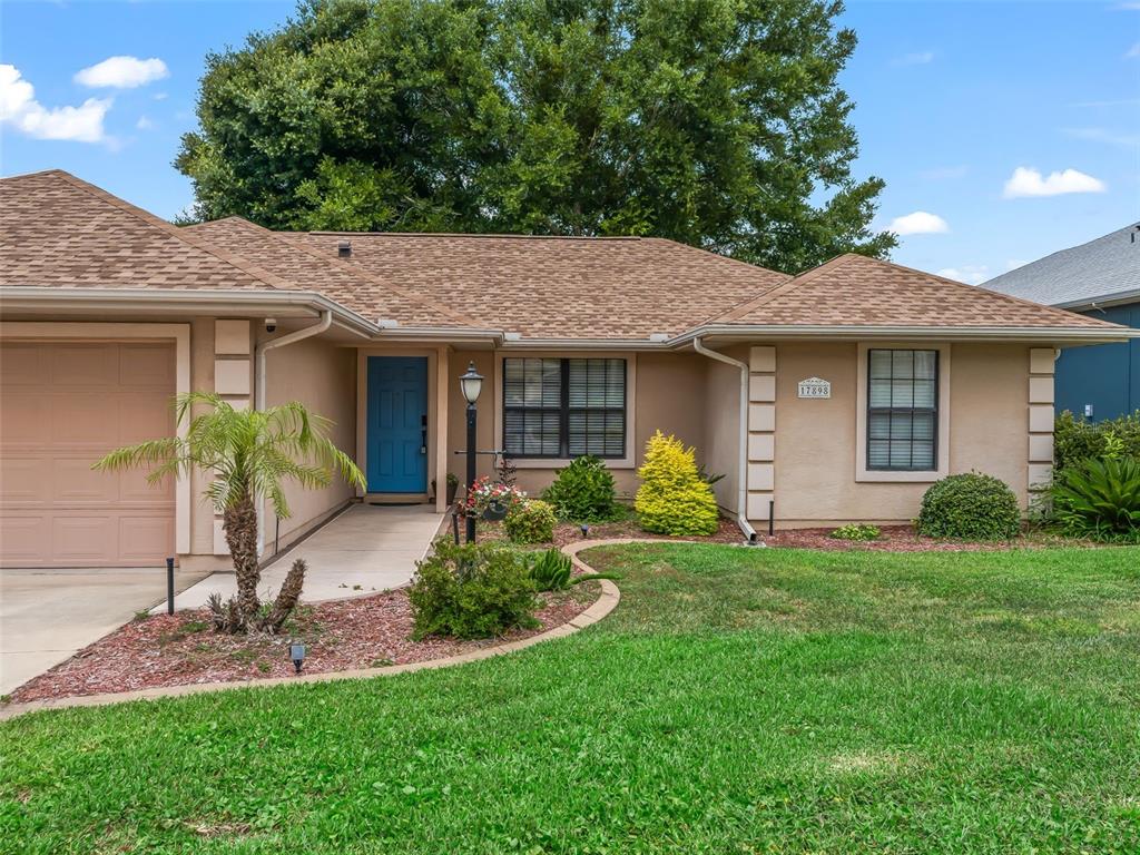 A single-story house with a tan stucco exterior, a blue front door, and a brown roof — 17898 SE 125TH CIRCLE, SUMMERFIELD, FL