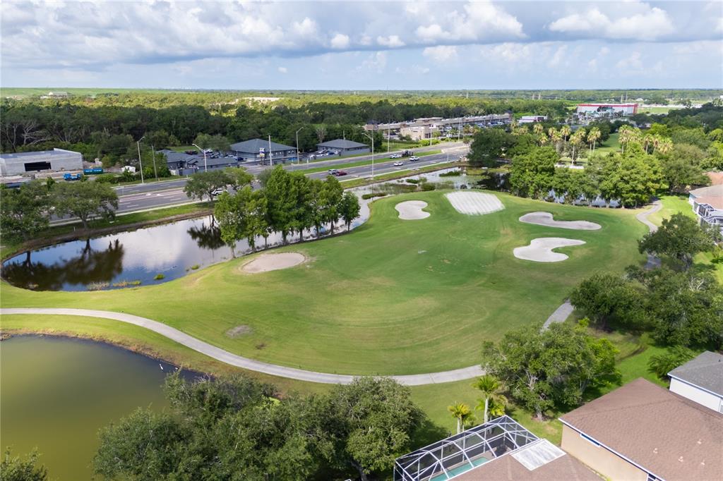 An aerial view shows a golf course fairway with sand bunkers, ponds, and surrounding trees — 1415 MILLBROOK CIRCLE, BRADENTON, FL