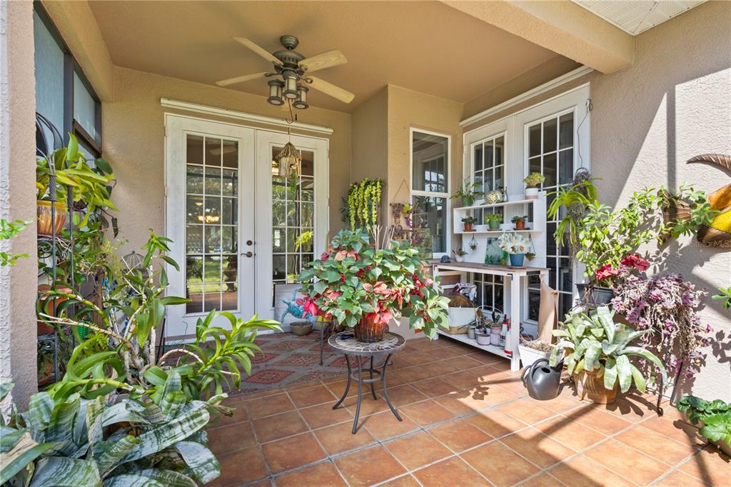 A covered patio features tiled flooring, a ceiling fan, French doors, and numerous potted plants — 1415 MILLBROOK CIRCLE, BRADENTON, FL