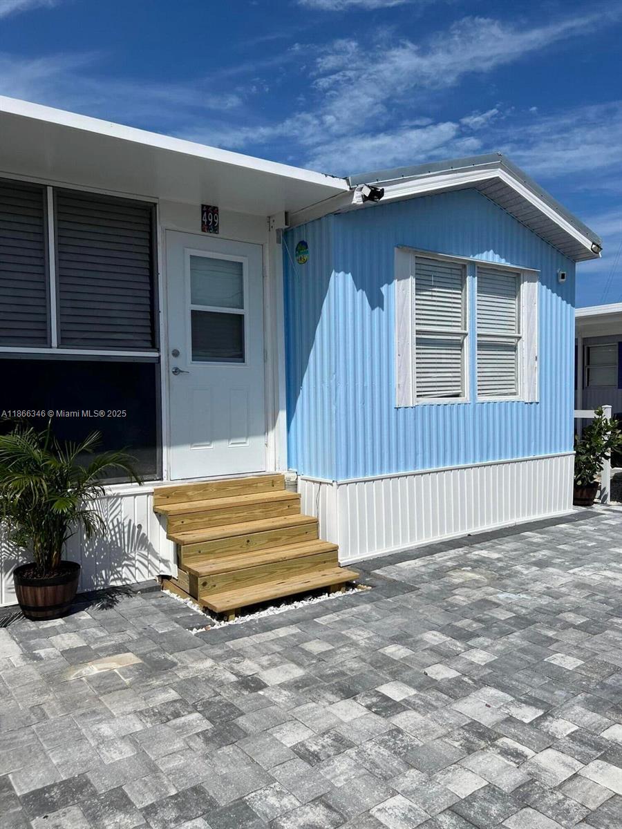 A light blue mobile home features a white door, wooden steps, and a paved patio — 325 Calusa St #499, Key Largo FL 33037, KEY LARGO, FL