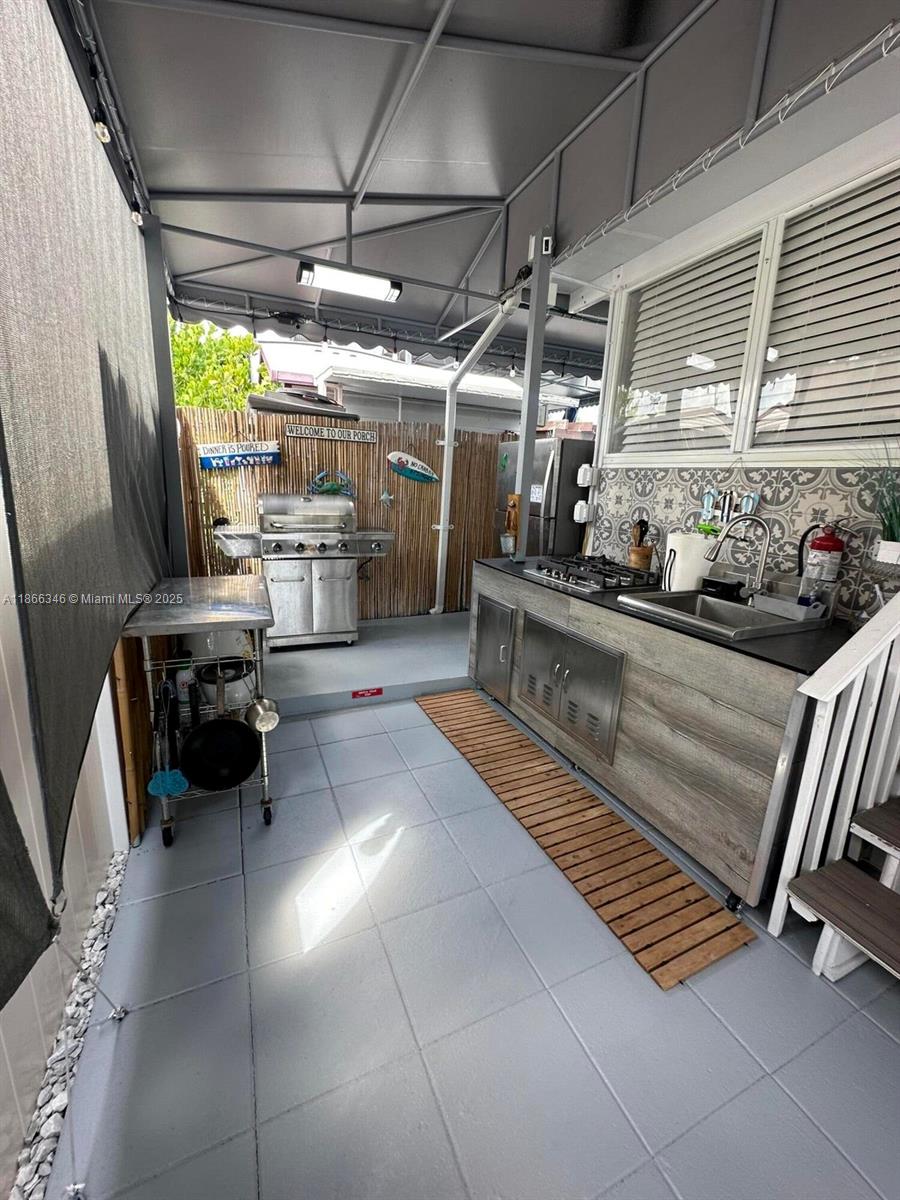 An outdoor kitchen features a stainless steel grill, a sink, and gray tile flooring — 325 Calusa St #499, Key Largo FL 33037, KEY LARGO, FL