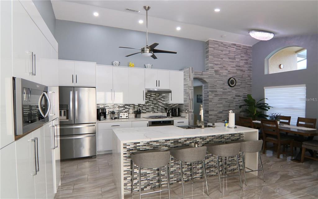 A modern kitchen features white cabinets, a marble-topped island, and a stone-tiled accent wall — 1470 WEDGE WAY, HAINES CITY, FL