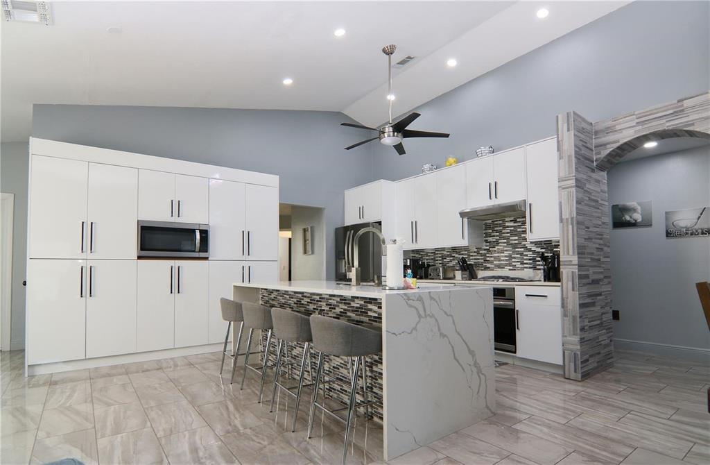A modern kitchen features white cabinetry, a marble-topped island with bar seating, and tiled floors — 1470 WEDGE WAY, HAINES CITY, FL