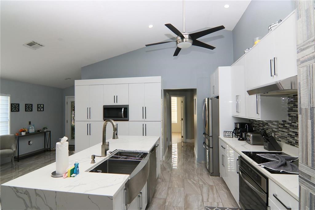 A modern kitchen features white cabinetry, a marble-topped island with a farmhouse sink, and tile flooring — 1470 WEDGE WAY, HAINES CITY, FL