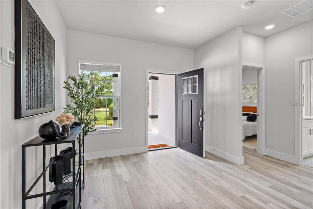 An entryway features light wood-look flooring, a dark front door, and a black console table — 3830 GARDENIA DRIVE, INDIAN LAKE ESTATES, FL