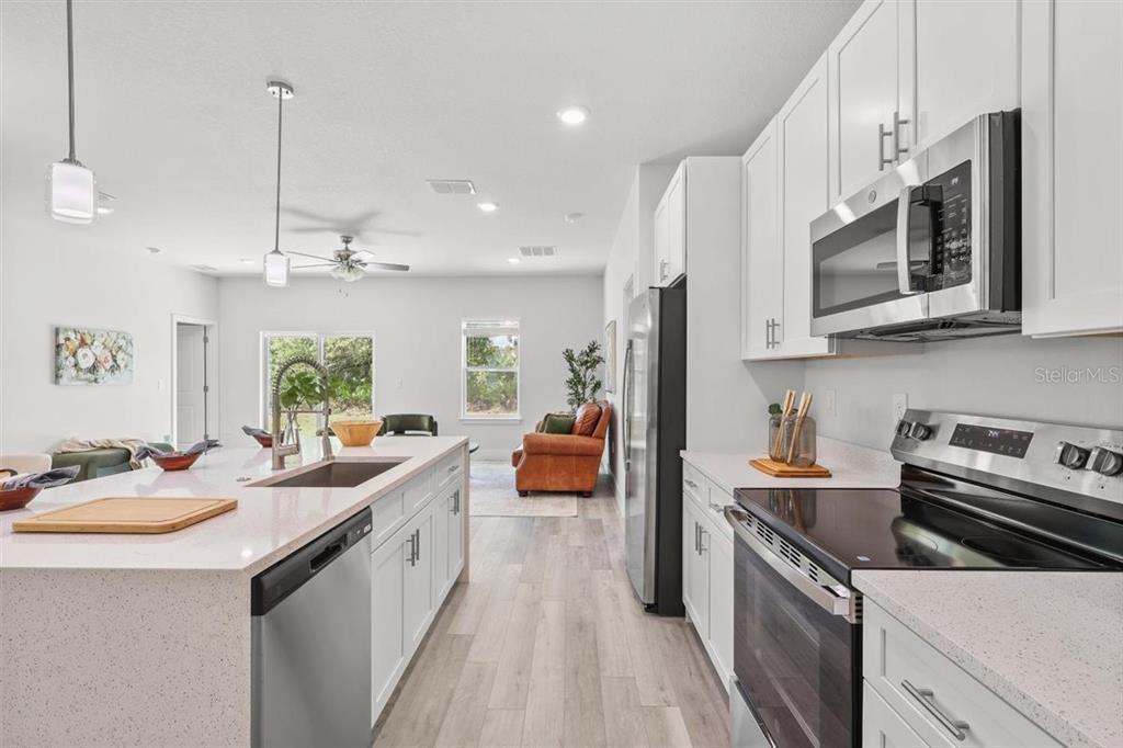 A modern kitchen with white cabinets, stainless steel appliances, and a large quartz island — 3830 GARDENIA DRIVE, INDIAN LAKE ESTATES, FL