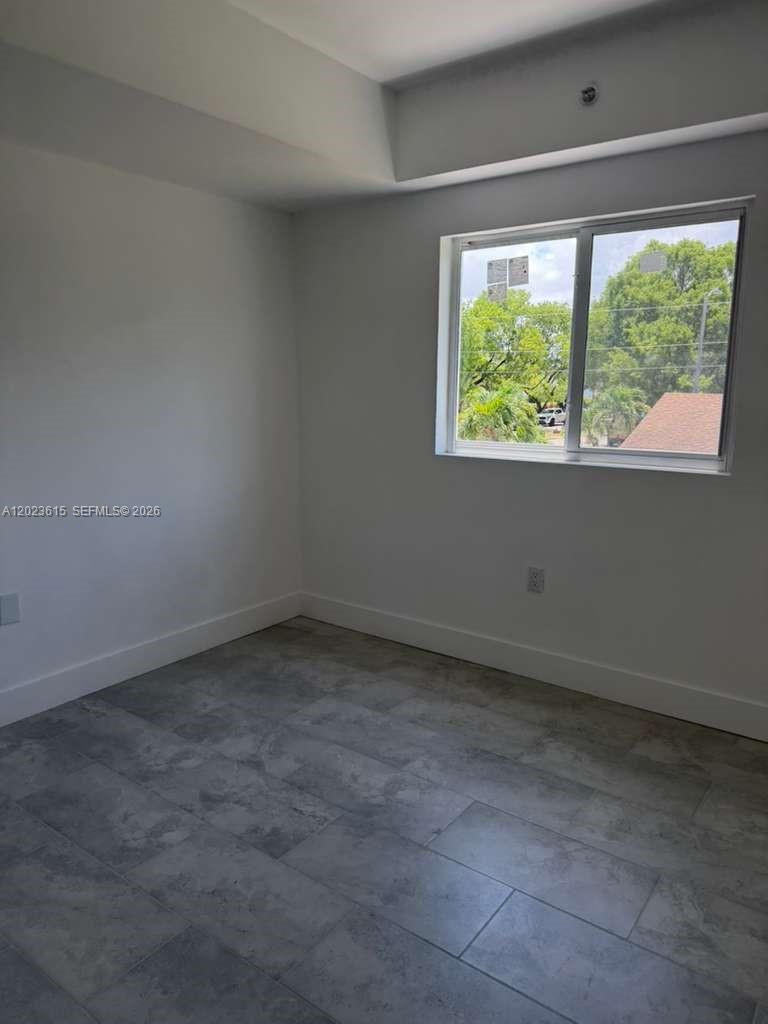 An empty room features light gray walls, large tile flooring, and a single window — 147 Nw 59th St # 302, Miami FL 33127, MIAMI, FL