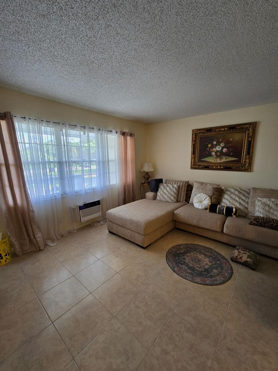A living room features a beige sectional sofa, tile flooring, and a window with curtains — 12 Prescott # 12, Deerfield Beach FL 33442, DEERFIELD BEACH, FL