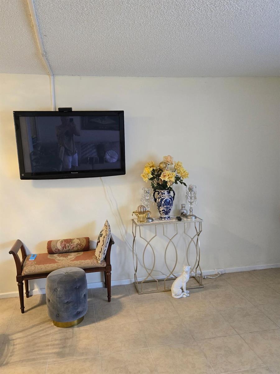 A wall-mounted television hangs above a small bench, a grey ottoman, and a metal console — 12 Prescott # 12, Deerfield Beach FL 33442, DEERFIELD BEACH, FL