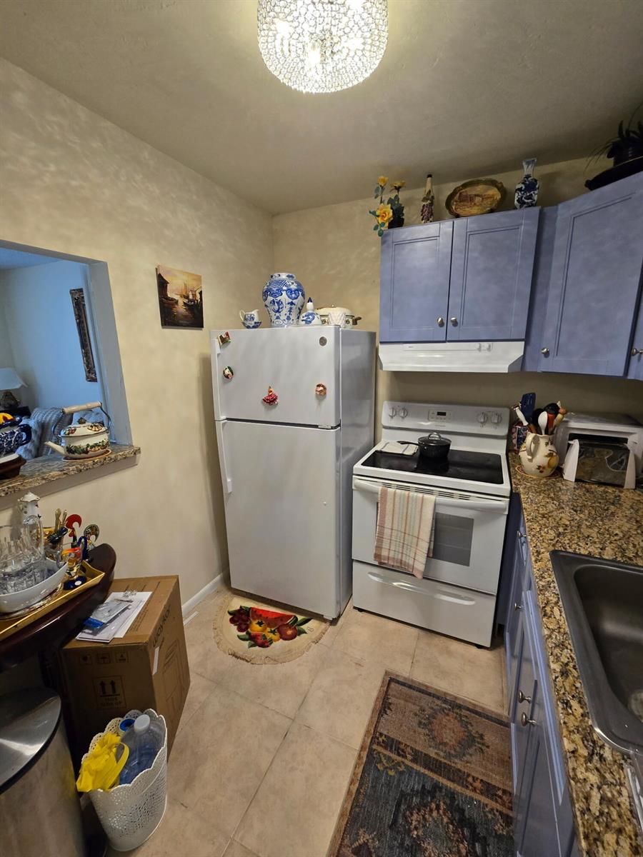 A kitchen features blue cabinets, granite countertops, a white refrigerator, and a white stove — 12 Prescott # 12, Deerfield Beach FL 33442, DEERFIELD BEACH, FL