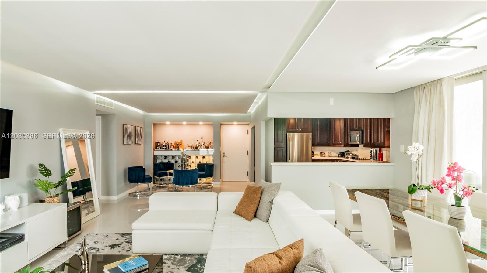 A modern living room features a white sectional sofa, a dining area, and a bar — 5750 Collins Ave # 7A, Miami Beach FL 33140, MIAMI BEACH, FL