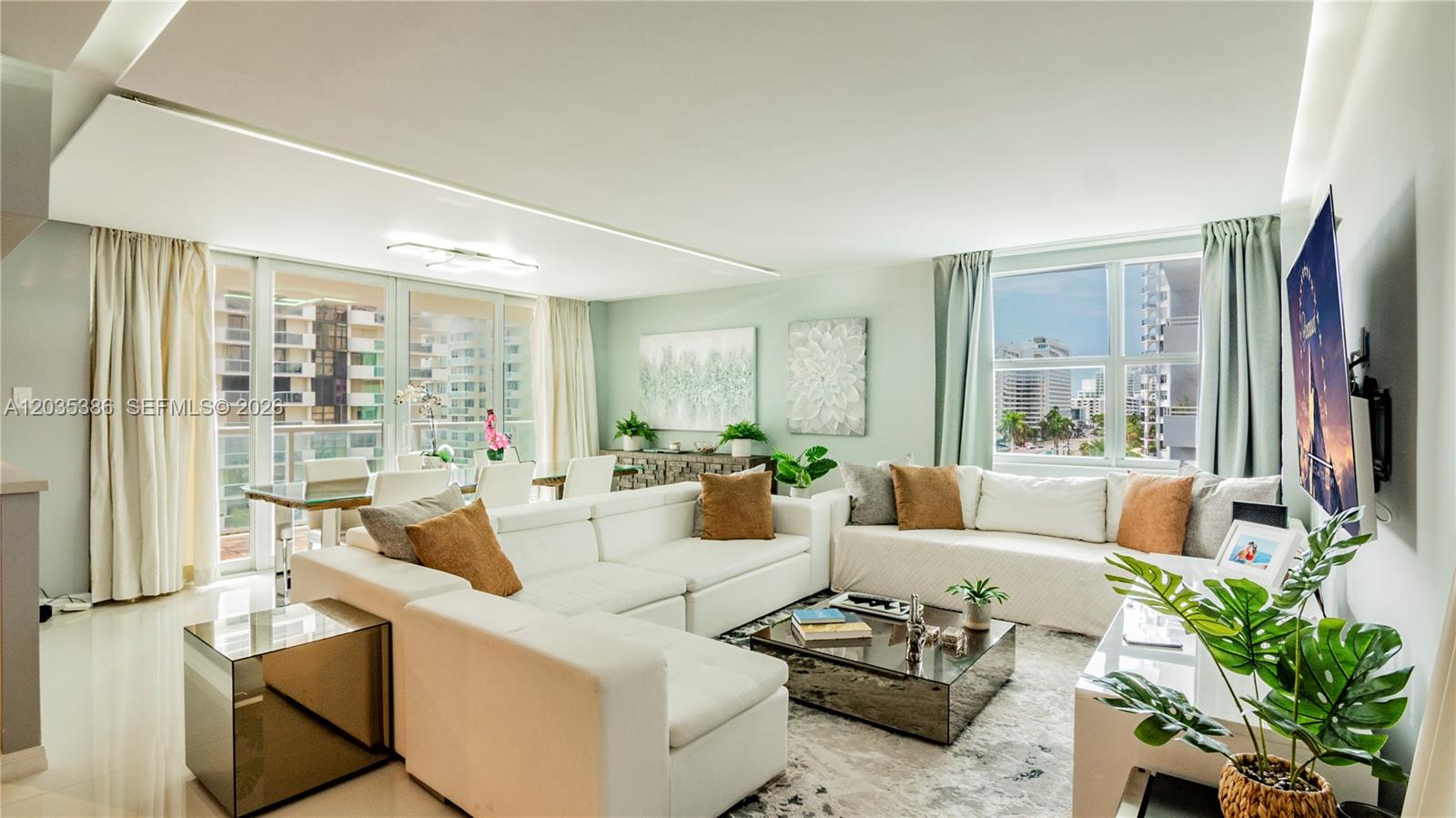 A bright living room features a large white sectional sofa, a glass coffee table, and floor-to-ceiling windows — 5750 Collins Ave # 7A, Miami Beach FL 33140, MIAMI BEACH, FL