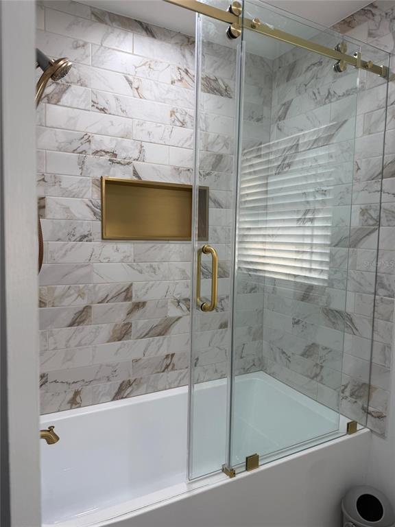 A bathtub and shower combination features marble-look tile walls, gold fixtures, and a glass door — 4534 N LAKE DRIVE, SARASOTA, FL