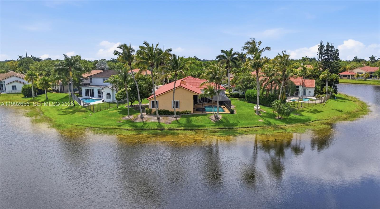 An aerial view shows a house with a red roof and pool beside a lake — 3038 Lakewood Dr, Weston FL 33332, WESTON, FL