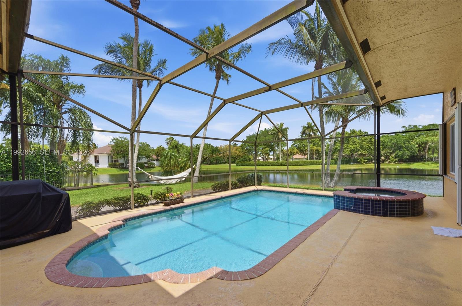 A screened-in patio features a swimming pool, a raised spa, and a view of a lake — 3038 Lakewood Dr, Weston FL 33332, WESTON, FL