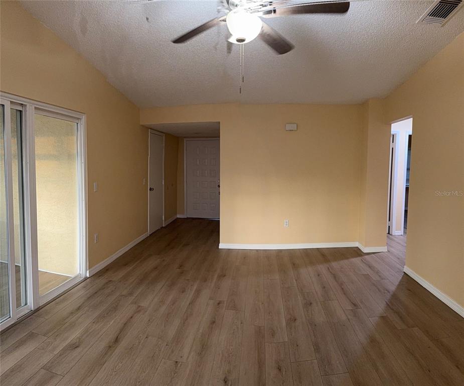 An empty living room features light-colored walls, wood-look flooring, a ceiling fan, and sliding doors — 1002 OROPESA AVENUE, ORLANDO, FL