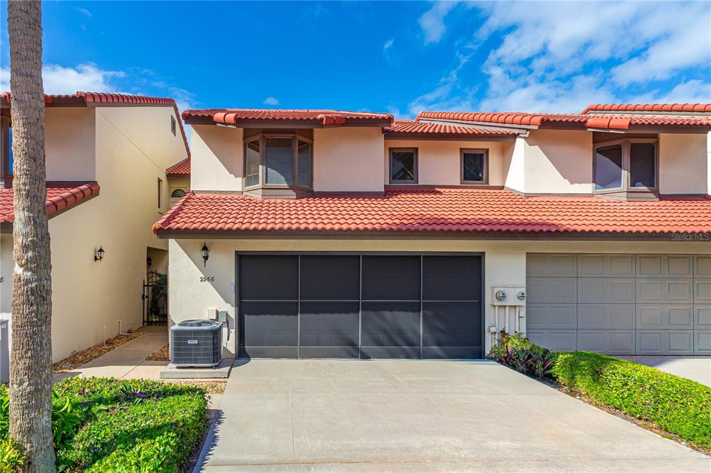A two-story townhouse exterior features a red tile roof, a dark garage screen, and beige stucco — 2966 OCEANS TRACE, DAYTONA BEACH SHORES, FL