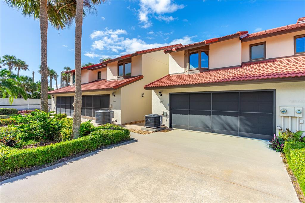 A two-story townhouse exterior features a concrete driveway, a garage, and a red tile roof — 2966 OCEANS TRACE, DAYTONA BEACH SHORES, FL
