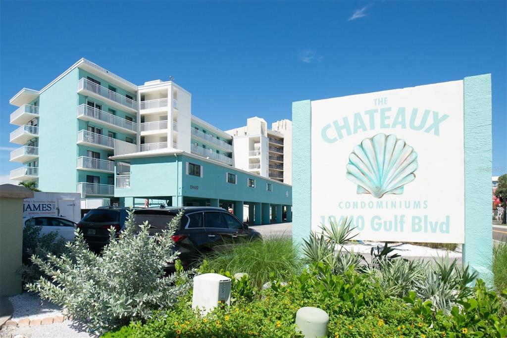 The exterior of a multi-story teal condominium building with a prominent sign in the foreground — 19440 GULF BOULEVARD UNIT 209, INDIAN SHORES, FL