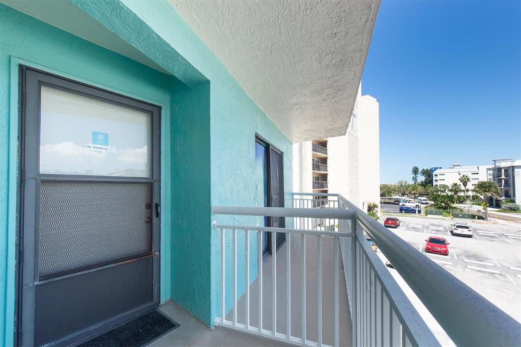 A turquoise balcony with a screen door overlooks a parking lot and nearby buildings — 19440 GULF BOULEVARD UNIT 209, INDIAN SHORES, FL