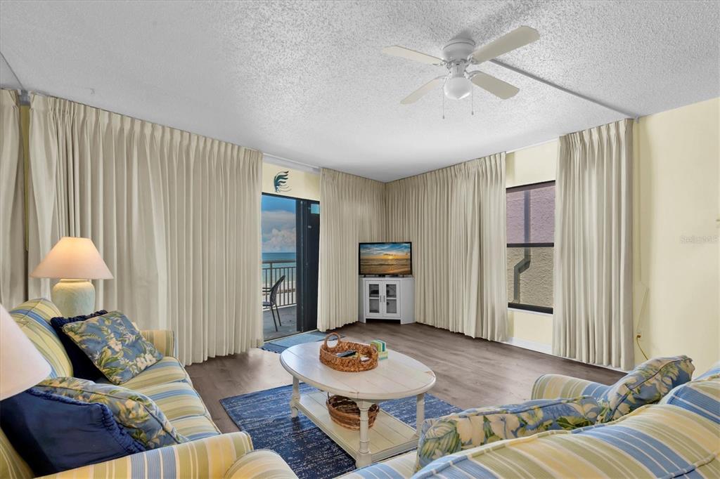 A living room features striped sofas, a coffee table, and a balcony with ocean views — 19440 GULF BOULEVARD UNIT 209, INDIAN SHORES, FL
