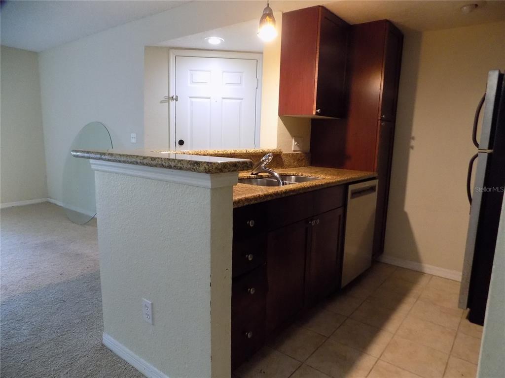 A kitchen features dark wood cabinets, granite countertops, a stainless steel sink, and tile flooring — 5116 CONROY ROAD UNIT 16, ORLANDO, FL