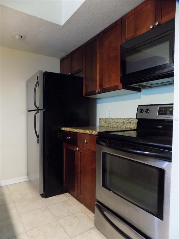 A kitchen features dark wood cabinets, stainless steel appliances, and granite countertops — 5116 CONROY ROAD UNIT 16, ORLANDO, FL