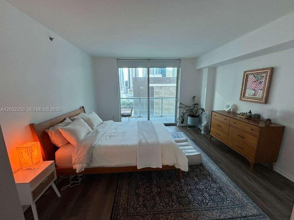 A bedroom features a bed, a wooden dresser, a patterned rug, and a balcony door — 55 SE 6th St # 1208, Miami FL 33131, MIAMI, FL