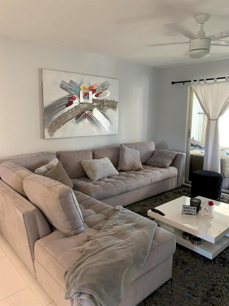 A living room features a gray sectional sofa, a white coffee table, and abstract wall art — 2500 Fiore Way # 109, Delray Beach FL 33445, DELRAY BEACH, FL