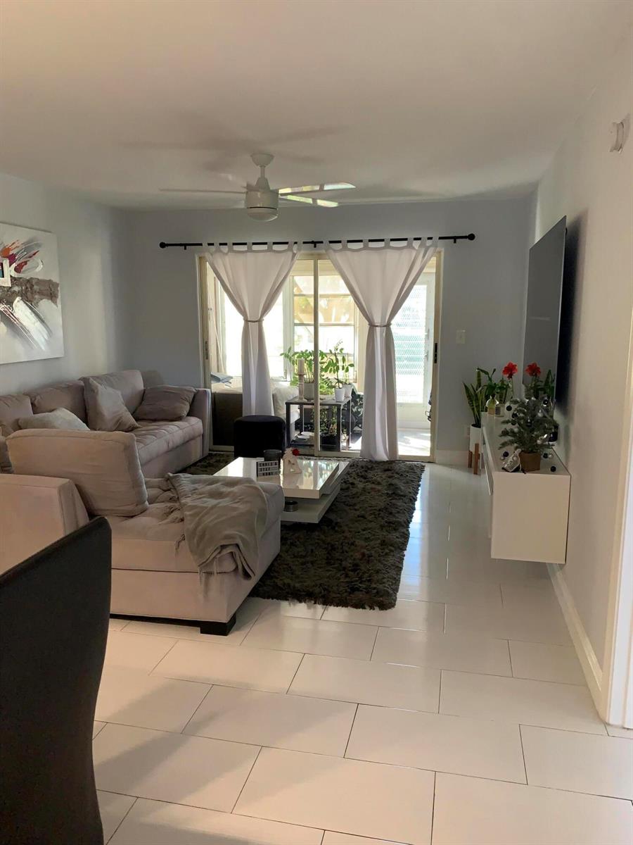 A living room features a grey sectional sofa, a dark rug, and a sliding glass door — 2500 Fiore Way # 109, Delray Beach FL 33445, DELRAY BEACH, FL
