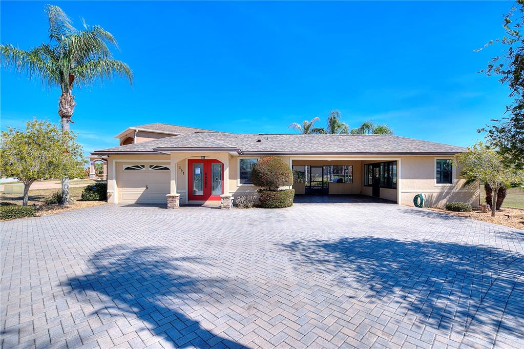 A single-story house with a red front door, a garage, and a large paved driveway — 561 MEANDERING WAY, POLK CITY, FL