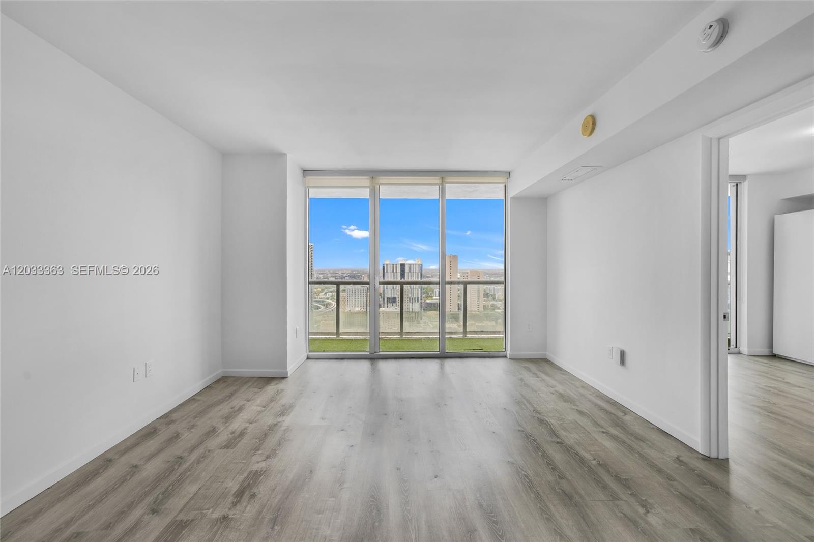 An empty room features light wood-look flooring, white walls, and floor-to-ceiling windows with city views — 50 Biscayne Blvd # 4307, Miami FL 33132, MIAMI, FL