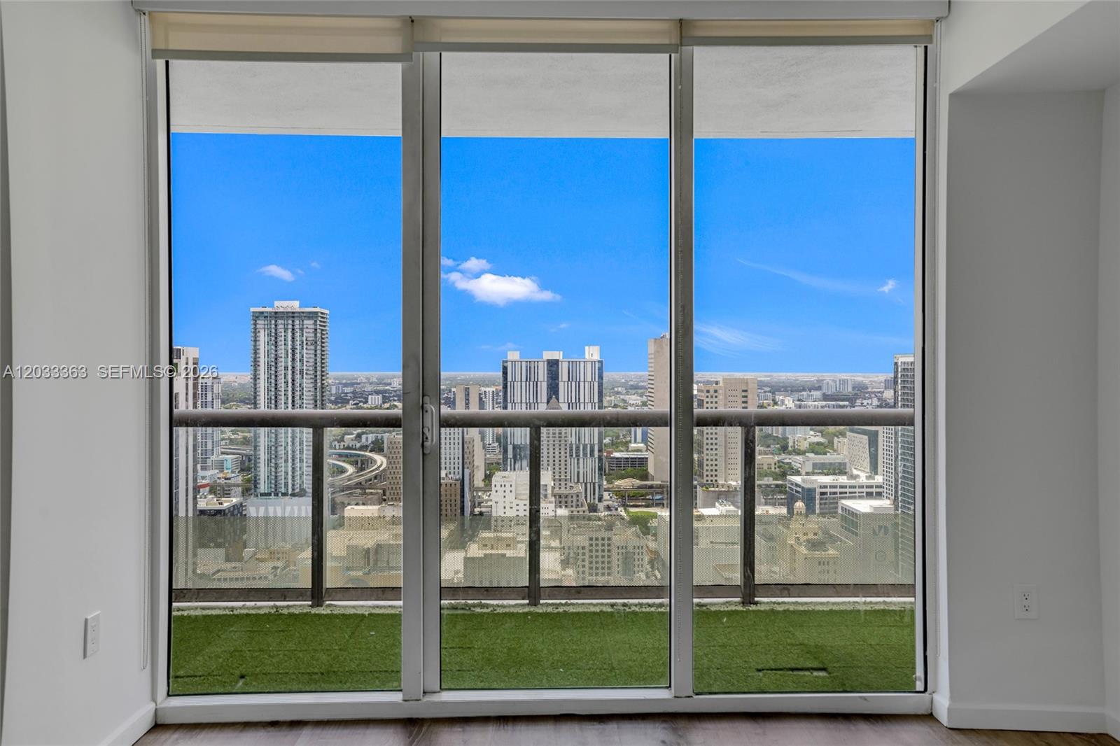 A view of a city skyline from a balcony with artificial turf through sliding glass doors — 50 Biscayne Blvd # 4307, Miami FL 33132, MIAMI, FL