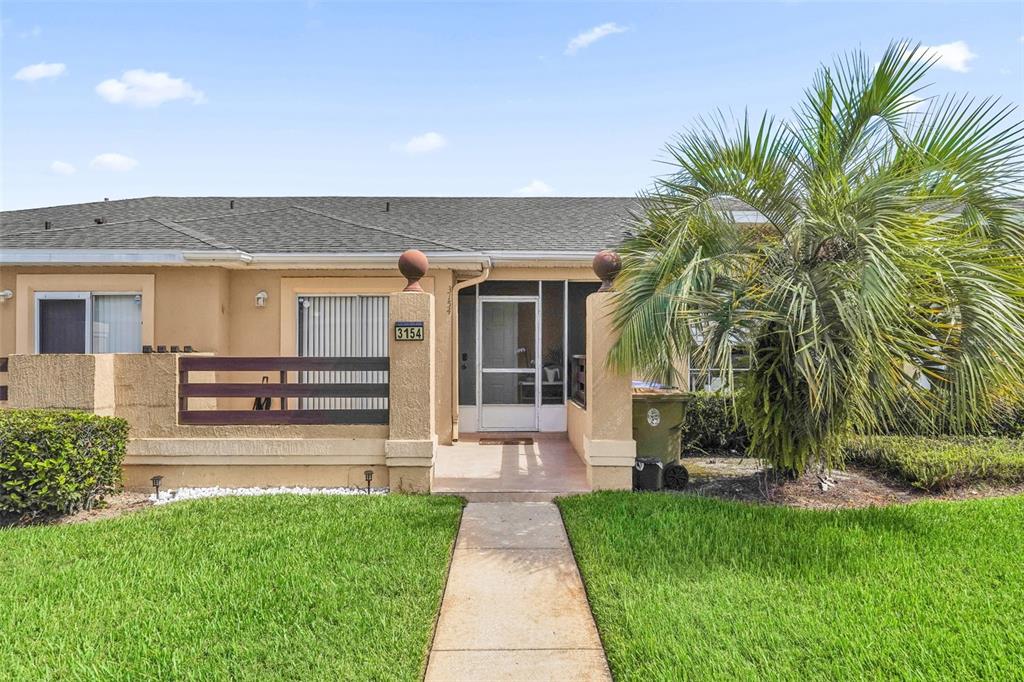 A single-story tan stucco home features a front walkway, a screen door, and a palm tree — 3154 SANDY SHORE LANE, KISSIMMEE, FL