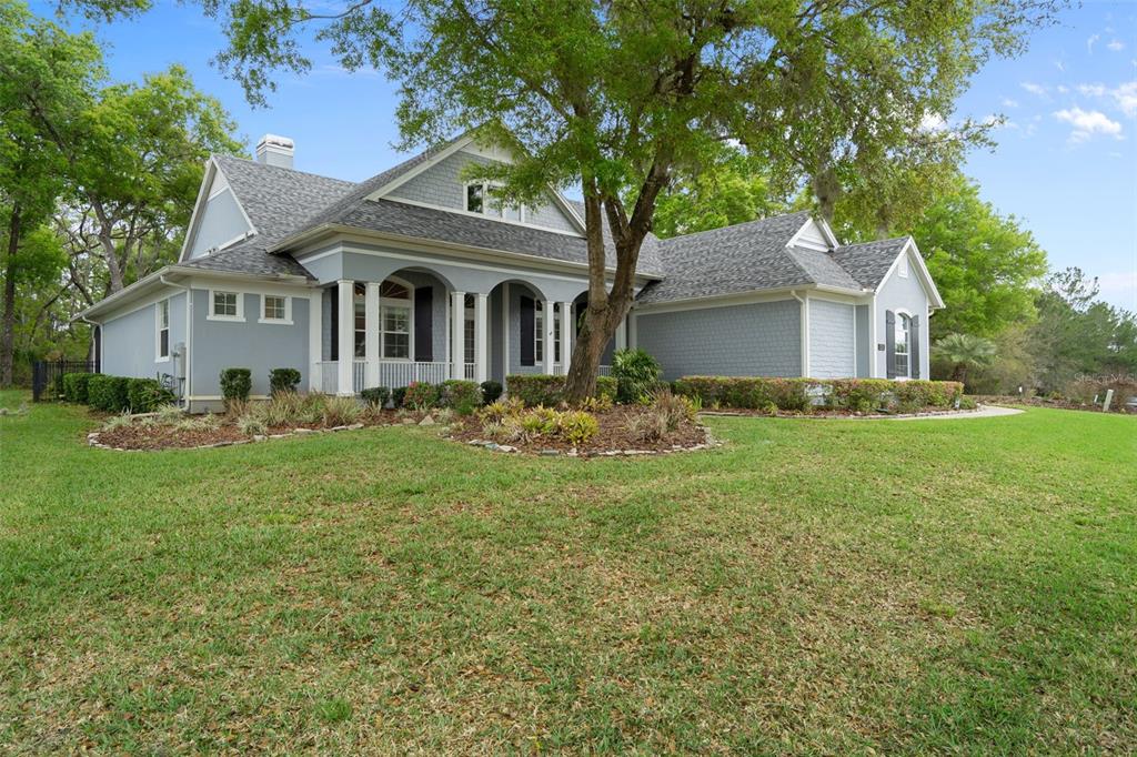 A gray, two-story house with a covered front porch and shingled roof sits on grass — 6096 DUSK ROSE LANE, BROOKSVILLE, FL