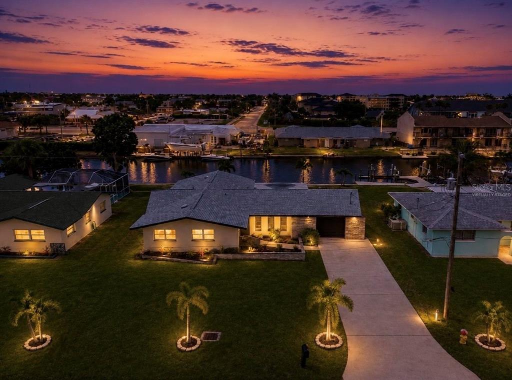 An aerial view of a waterfront house at sunset with a lawn and palm trees — 1729 BIKINI COURT, CAPE CORAL, FL