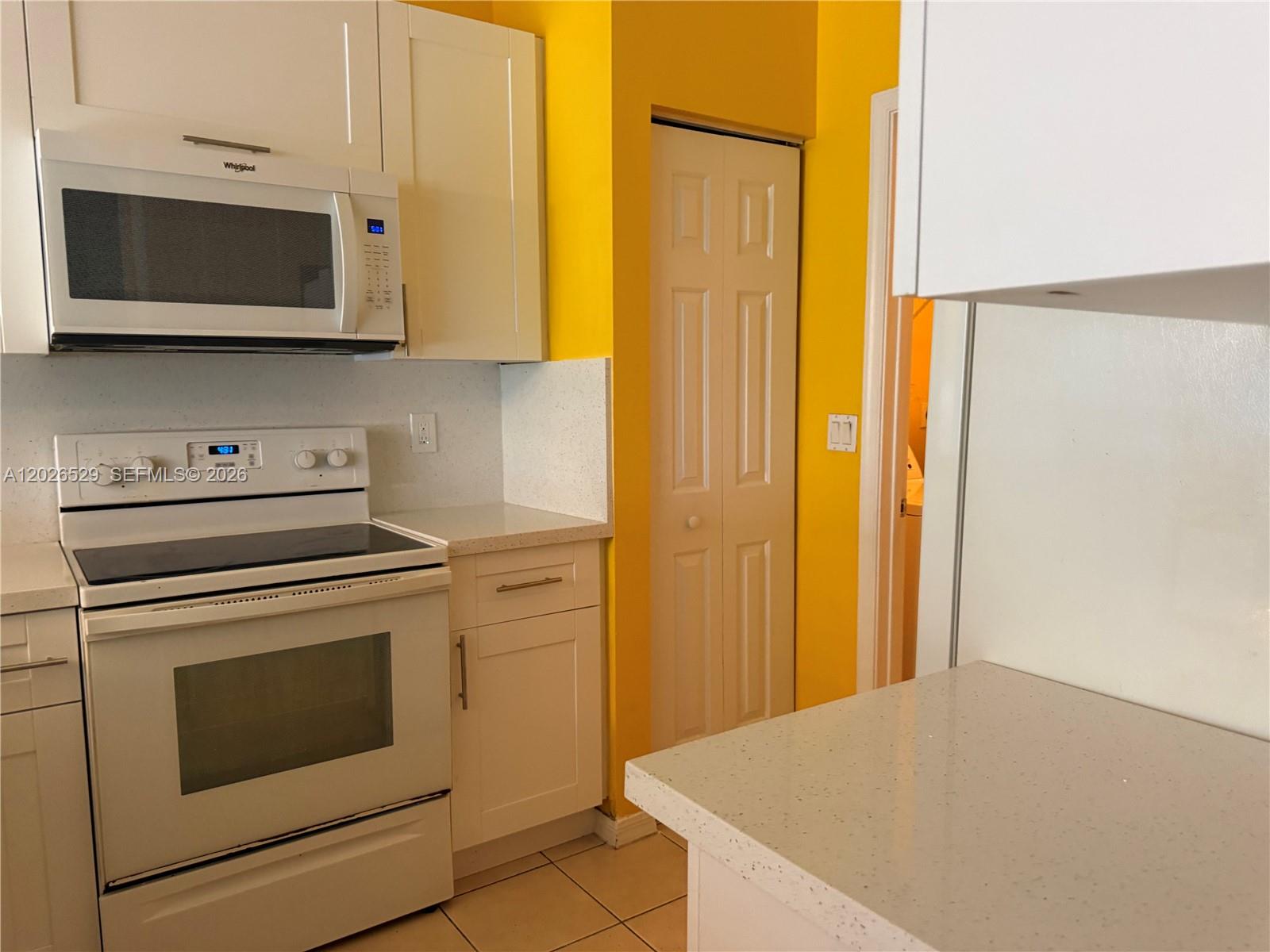 A kitchen features white cabinets, a white stove, a microwave, and bright yellow walls — 4951 Mallory St # 4951, Lake Worth FL 33463, LAKE WORTH, FL