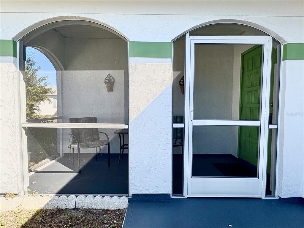 A screened-in porch features arched openings, a green front door, and a dark floor — 8181 MARLOW COURT, NORTH PORT, FL