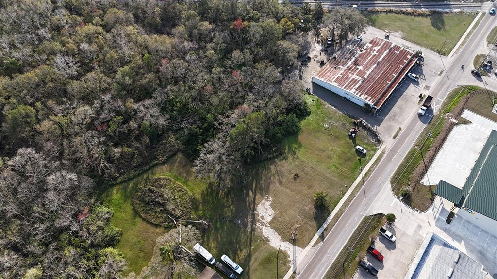 An aerial view shows a vacant lot adjacent to commercial buildings and a wooded area — 713 E ALSOBROOK STREET, PLANT CITY, FL