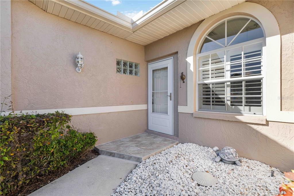 A front entryway with a white storm door, arched window, and decorative stone turtle — 5064 MAHOGANY RUN AVENUE, SARASOTA, FL