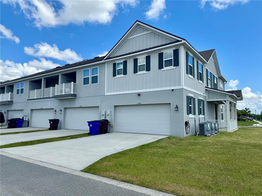 A multi-story townhouse building features gray siding, white trim, and multiple attached garages — 2540 BLOWING BREEZE AVENUE, KISSIMMEE, FL