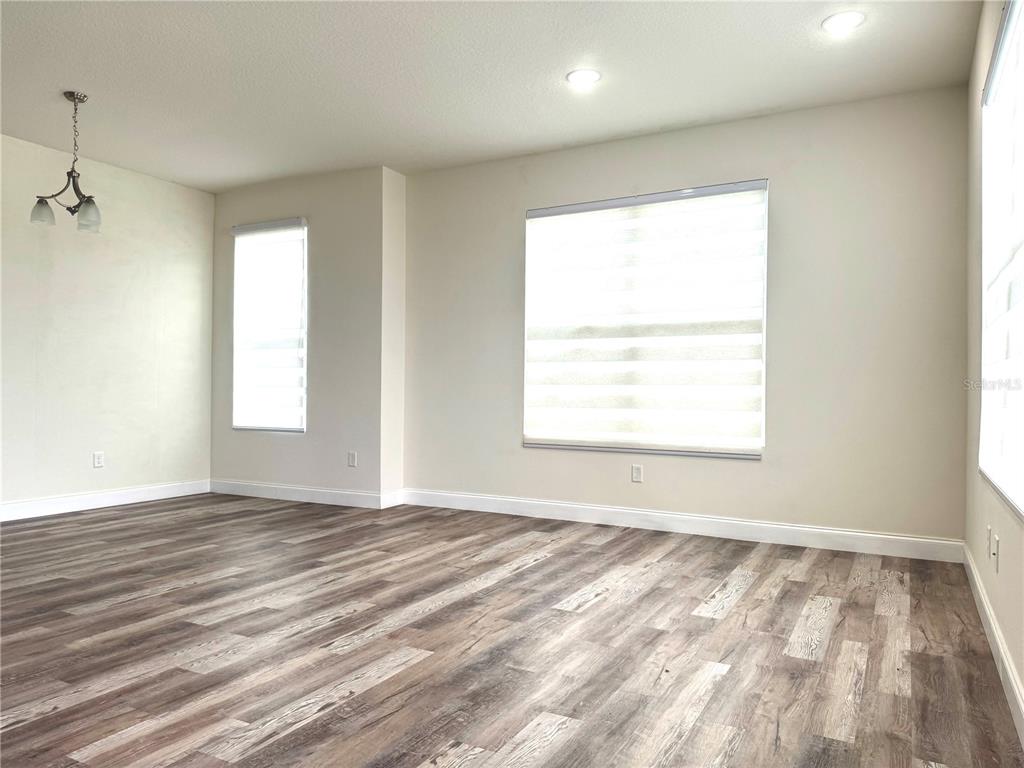 An empty room features light-colored walls, wood-look flooring, recessed lighting, and multiple windows with blinds — 2540 BLOWING BREEZE AVENUE, KISSIMMEE, FL