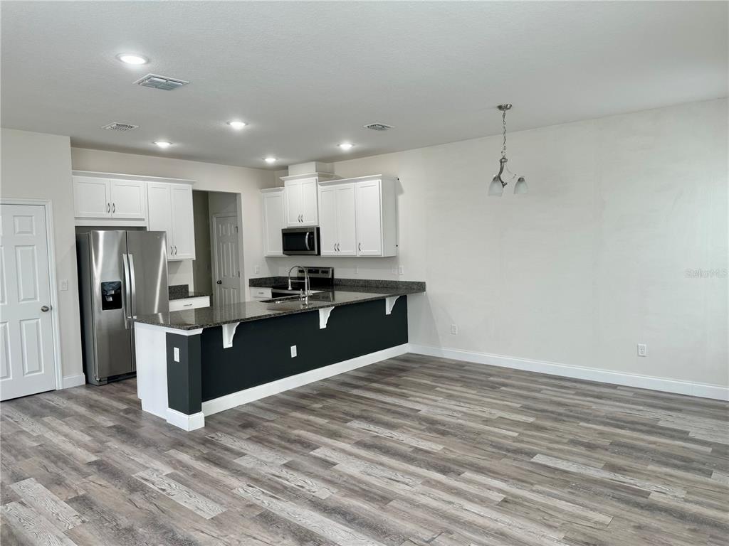 A kitchen with white cabinets, dark countertops, and a breakfast bar overlooks a living area — 2540 BLOWING BREEZE AVENUE, KISSIMMEE, FL